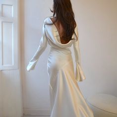 a woman in a white dress is standing near a wall and looking at the floor