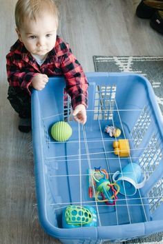 a toddler playing with toys in a blue plastic toy tray on the floor at home