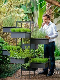 a man standing next to a tall planter filled with grass and plants in it