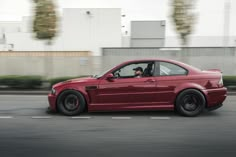 a red car driving down the road with it's driver in the passenger seat