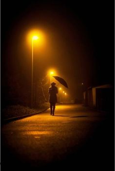 a person with an umbrella walking down the street at night