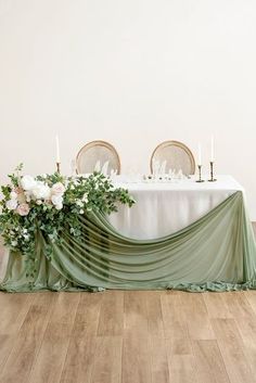 the table is set with white flowers and greenery on it, along with candles