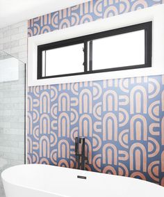 a bath tub sitting under a window next to a tiled wall with geometric designs on it