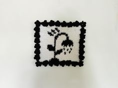 a crocheted square with a black and white design on the bottom, in front of a white wall