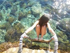 a woman sitting on top of a rock next to the ocean with her legs crossed