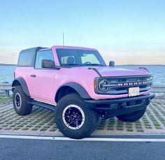 a pink pick up truck parked next to the ocean