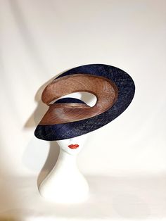 Hat Title: The Return  A spectacular sculptural construction using the finest of Abaca derived textiles, called PinokPok.  The architectural swirl shape of this hat is made up of two layers. The outer layer is in navy colour matching the hat base.  The inner layer is made up of multiple strands of fibre in various shades, which together add a luminous shine to the resulting end weave.  It's rather difficult to describe this colour but you can see fibres in shades of navy, copper/orange, beige, etc. To get a better idea of the colour and also to truly appreciate this multi-strand weave, take a look at the closeup images and watch the video.  The hat adheres to your head via custom made wire prongs or a millinery elastic (whichever works best). British Hats, Ivory Hat, Elegant Hat, Navy And Copper, Racing Fashion, Red Fascinator, Royal Ascot Hats, Rose Hat, Luxury Hats