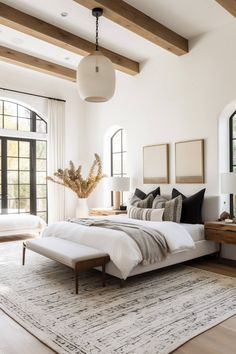 a large bedroom with white walls and wood beams on the ceiling is decorated in neutral tones