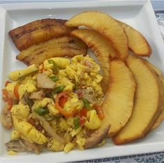 a white plate topped with eggs, meat and veggies next to sliced pineapple slices