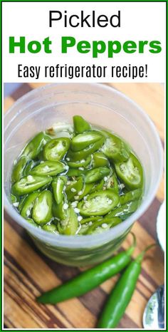 pickled hot peppers in a glass bowl on top of a wooden table next to green peppers