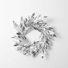 a silver wreath with leaves on it sitting on a white surface next to a wall