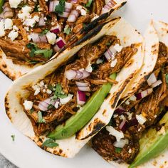 three tacos with shredded meat, onions and green peppers on a white platter