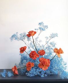 an arrangement of orange and blue flowers in a vase on a black table with white background