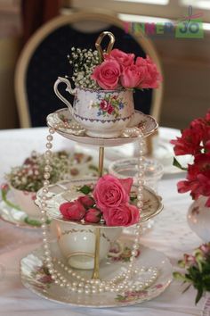 three tiered cake stand with pink roses and pearls on the top, sitting on a table