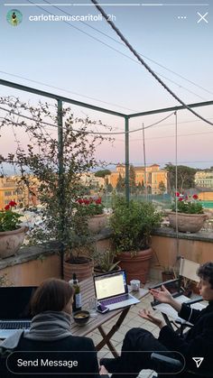 two people sitting at a table on top of a roof with laptops in front of them