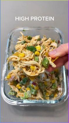 a hand holding a spoon full of chicken and veggies in a glass dish