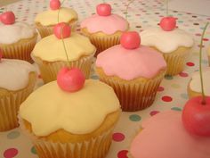 cupcakes with white frosting and pink icing topped with cherries on a polka dot tablecloth