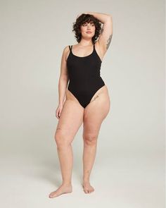 a woman in a black one piece swimsuit posing for the camera with her arms behind her head