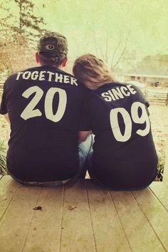 two people sitting back to back wearing black shirts with white letters on them, facing each other