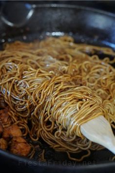 noodles being cooked in a pan with wooden spoon