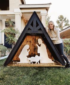 a woman standing next to a nativity scene in front of a house with christmas lights