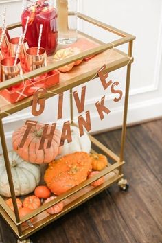 a gold serving cart filled with drinks and pumpkins on top of a hard wood floor