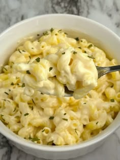 a white bowl filled with macaroni and cheese on top of a marble counter