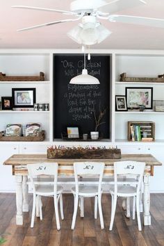 a dining room table with white chairs and a chalkboard on the wall