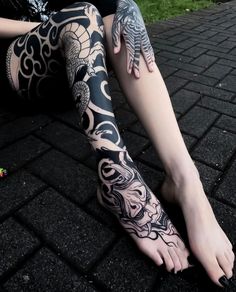 a woman sitting on the ground with her legs covered in black and white tattoo designs