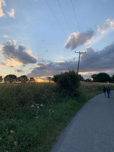 two people are walking down the road in front of some power lines and trees at sunset