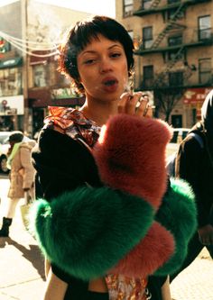 a woman is walking down the street with her hand in her mouth and wearing a fur coat