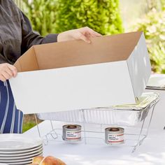 a person holding a box with food in it on top of a table next to plates and bowls