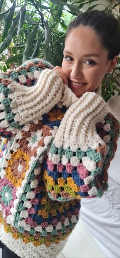 a woman wearing a multicolored crocheted sweater and holding her hand on her shoulder