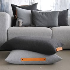 a couch with pillows on top of it in front of a wall and floor lamp