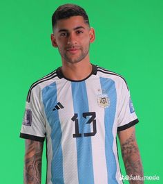 a man with tattoos standing in front of a green background wearing a blue and white striped shirt