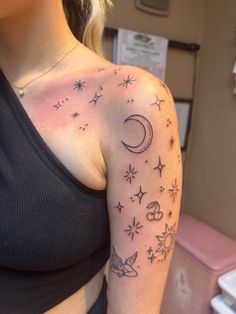 a woman wearing a black top with stars and moon tattoos on her arm, in front of a mirror