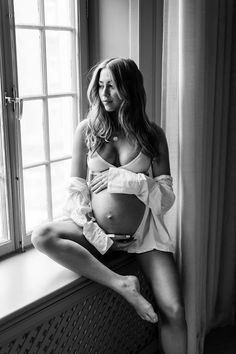 a pregnant woman sitting on a window sill with her belly wrapped around her waist