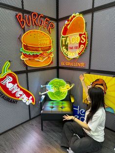 a woman sitting on the floor in front of some neon signs and tacos