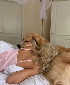 a woman laying in bed next to a large dog with her head on the pillow