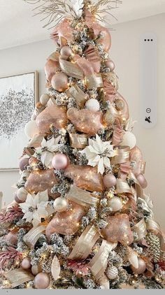 a decorated christmas tree with pink and gold ornaments on it's top, in a living room