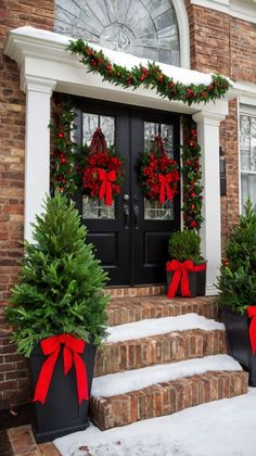 two christmas wreaths are on the front steps of a house with red bows and evergreen trees