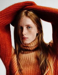 a woman in an orange sweater poses with her hands on her head