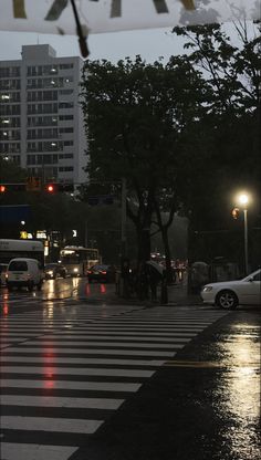 a city street at night with cars and people crossing the street in the rain under an umbrella