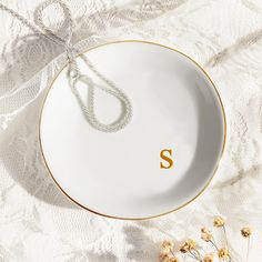 a plate with the letter s on it next to some dried flowers and a chain