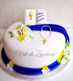 a white cake with blue ribbon and yellow flowers on the top is decorated with an open book