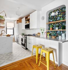 a kitchen with white cabinets and yellow stools in front of an island countertop