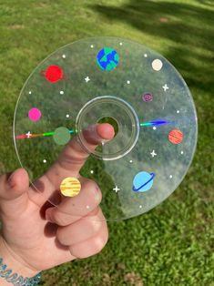 a hand holding a clear disc with planets and stars on it in front of grass