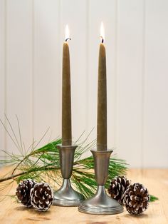 two candles are sitting next to pine cones