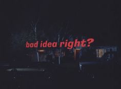 a neon sign that says bad idea right? in front of some parked cars at night