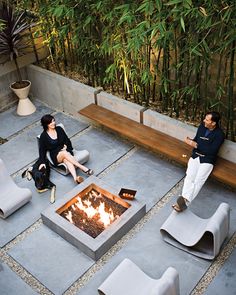 two people sitting around a fire pit in the middle of an outdoor area with chairs and tables